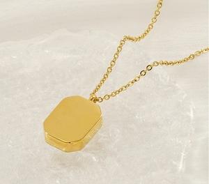 Detail of a polished gold-plated rectangular pendant on an O-chain over a glass tray
