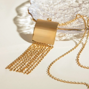 Detail of gold square pendant with long tassel chains on a textured glass tray