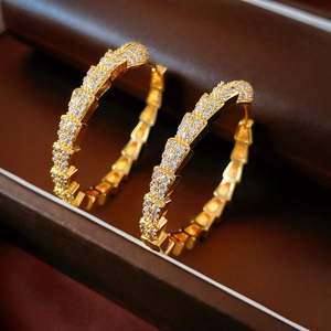 Macro shot of gold-plated geometric earrings with white zircon and snake scale texture