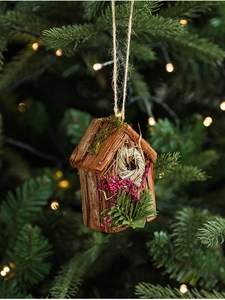 Détail d'un nichoir en écorce et mousse suspendu à un sapin de Noël illuminé