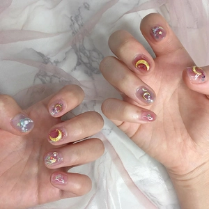 Detail of moon and star nail art with golden charms, pearls and glitter on marble background
