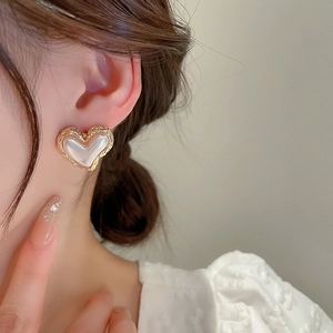 Close-up of heart-shaped gold textured earring with pearl inlay worn by a model