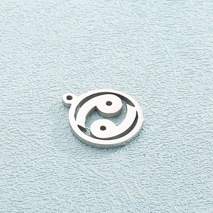 Silver stainless steel Yin Yang pendant with cutout design on blue textured surface