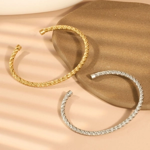 Makroaufnahme von gedrehten Gold- und Silberarmbändern auf strukturiertem Stein mit Schatten
