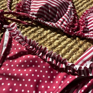 Détail d'un bikini bordeaux à pois et rayures avec volants sur un fond de paille tissée