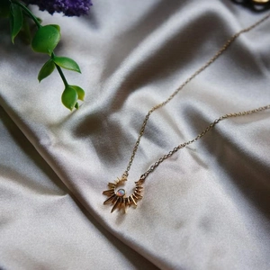 Elegant gold celestial sun pendant necklace with opal stone on grey silk fabric backdrop