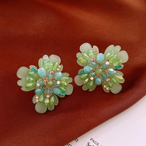 Détail de boucles d'oreilles fleuries vertes avec perles bleues et cristaux sur soie