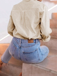 Detail of beige striped long-sleeve shirt tucked into light blue jeans with back label