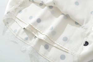 Close-up of white satin dress featuring dark grey polka dots and white lace trim