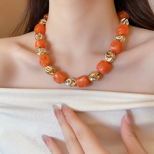 Close-up of chunky orange resin beads and irregular gold metal beads worn on the neck