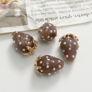 Detailed macro view of brown strawberry resin charms with white pearls and gold loops