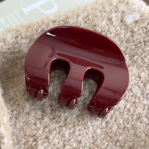 Macro shot of glossy red acrylic M-shaped hair claw clip on soft beige plush fabric