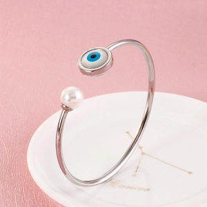 Macro shot of silver evil eye and pearl open bangle on a ceramic zodiac cancer tray