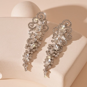 Macro detail of silver leaf tassel earrings with sparkling rhinestones on stone pedestal