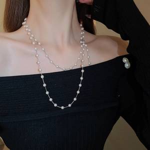 Détail d'un collier de perles superposées sur un haut en tricot noir et chaîne en argent