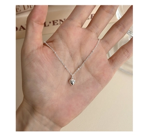 Close-up of hand holding a polished silver heart pendant necklace with beaded chain