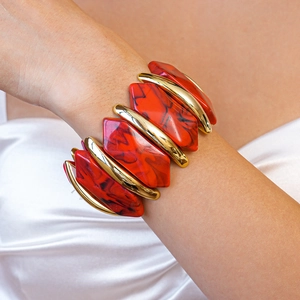 Gros plan d'un bracelet extensible en résine marbrée rouge et métal doré au poignet