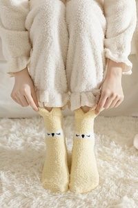 Detail showing yellow plush coral fleece socks with animal ear embroidery and closed eyes