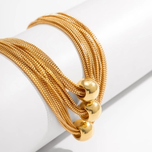 Close-up of layered gold chain bracelet with polished round beads on a white stand