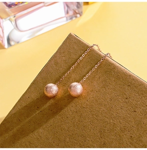 Detail of rose gold thread earrings with frosted bead hanging over a craft box