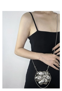 Close-up of a silver flower-shaped metal crossbody bag with a beaded chain on a model