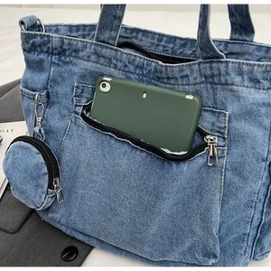 Close-up of blue denim tote bag featuring a front zipper pocket and a mini coin purse