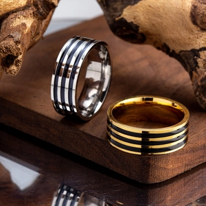 Wide 8mm stainless steel rings in silver and gold with black enamel stripe on wood base