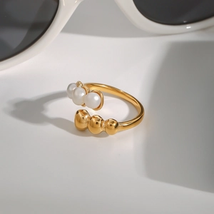 Gold plated open ring with three white pearls and metal beads on a white background