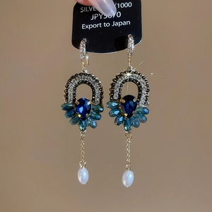 Détail de la boucle d'oreille en argent avec cristal bleu, pierres émeraudes et perle