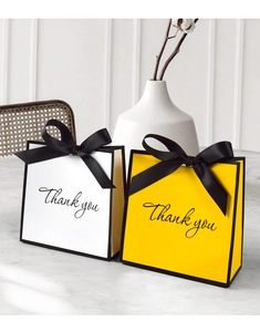 Detailed view of yellow and white gift bags with black satin bows on marble surface
