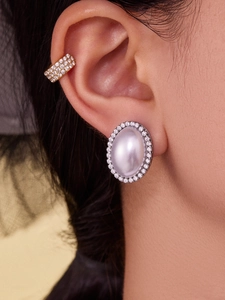 Close-up of elegant 18k gold oval pearl stud earrings with sparkling zircon accents on ear