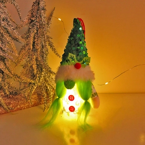 Lighted Christmas green gnome with sequin hat and braids near festive tree branches
