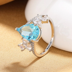 Macro close-up of pear-shaped blue gemstone ring with white crystals on gold fabric