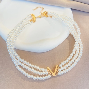 Détail d'un collier de perles à trois couches avec un pendentif doré en forme de V