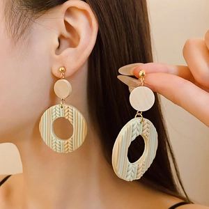 Close-up of beige geometric drop earrings with woven texture and gold metal rings on model