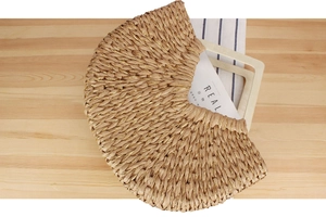 Detailed top view of a half-moon woven straw handbag with gold thread and wooden handle