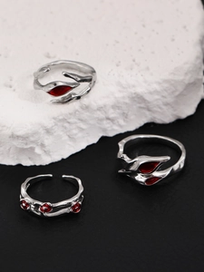 Macro shot of silver punk rings with red gems and thorn designs on dark volcanic rock