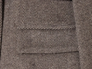 Detailed macro view of herringbone wool fabric texture and side pocket stitching on blazer