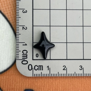 Macro shot of a small black resin star charm showing 1.5cm size on a metric ruler