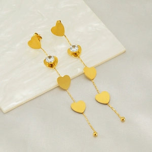 Golden heart drop earrings with zircon crystals on a minimalist textured surface