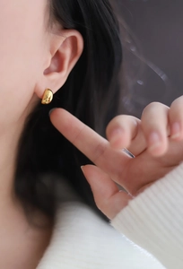 Macro view of polished gold oval stud earrings shown on model with shiny metallic finish