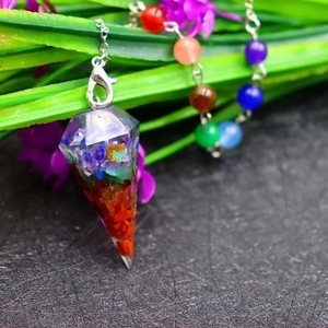 Detail of a seven-chakra resin pendulum with colorful crushed stones on a silver chain