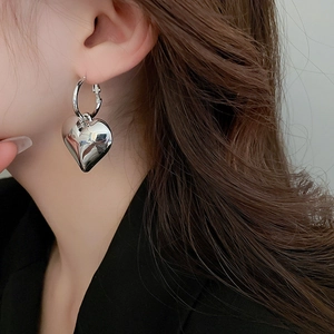 Close-up of polished silver heart dangle earring worn by a model in a side profile view