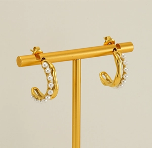 Detailed view of 18K gold-plated C-shaped earrings with inlaid white pearls on a stand
