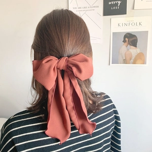 Detailed view of a brick red bow hair tie worn on a ponytail with elegant fabric streamers