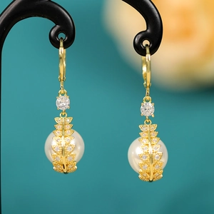 Close-up of pearl drop earrings with gold leaf patterns and sparkling zircon details