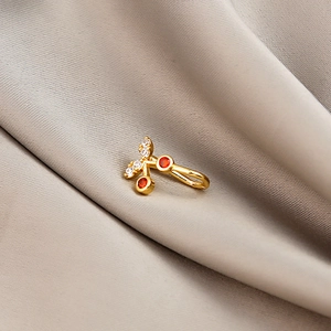 Macro shot of a golden cherry nose ring featuring red stones and clear crystal leaf details