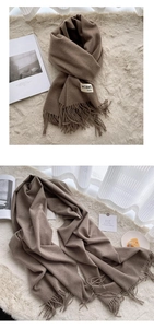 Detailed close-up of a brown cashmere feel scarf with fringe on a beige rug