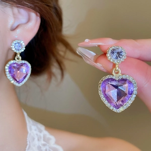 Détail des boucles d'oreilles cœur violet avec strass brillants et finition dorée
