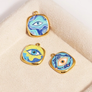 Detailed macro view of three gold-plated enamel devil eye pendants on beige velvet